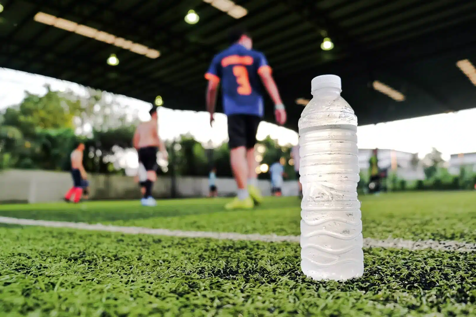 Fußballfeld mit Spielern, im Vordergrund steht eine Wasserflasche.