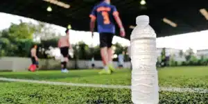 Fußballfeld mit Spielern, im Vordergrund steht eine Wasserflasche.