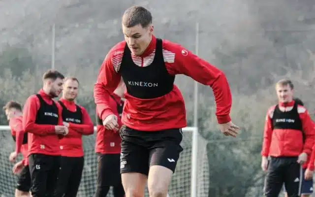 Eine Mannschaft, alle in schwarz-rot gekleidet, führt das Performance Tracking durch. Ein Spieler im Vordergrund sprintet mit Ball.